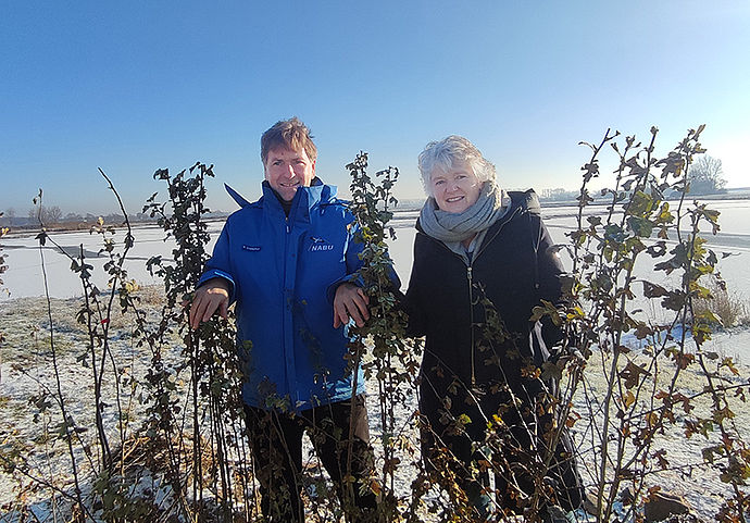 Ein mann und eine Frau vor einer winterlichen Kulisse mit weißen weiden stehen mitten in einer Hecke mit Jungpflanzen