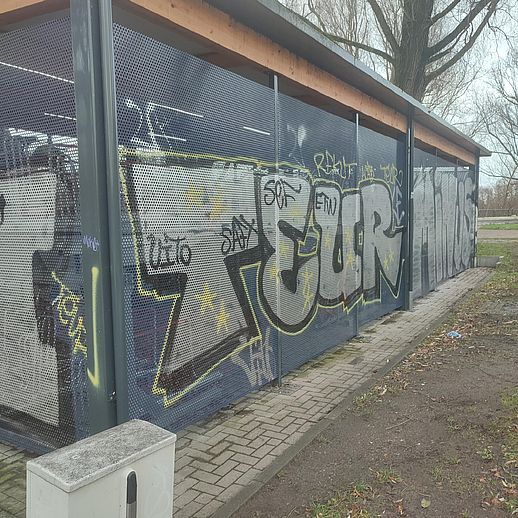 Das Bild zeigt eine vergitterte Anlage für Fahrräder, die unter anderem mit dem Tagg "TEURO" versehen ist.