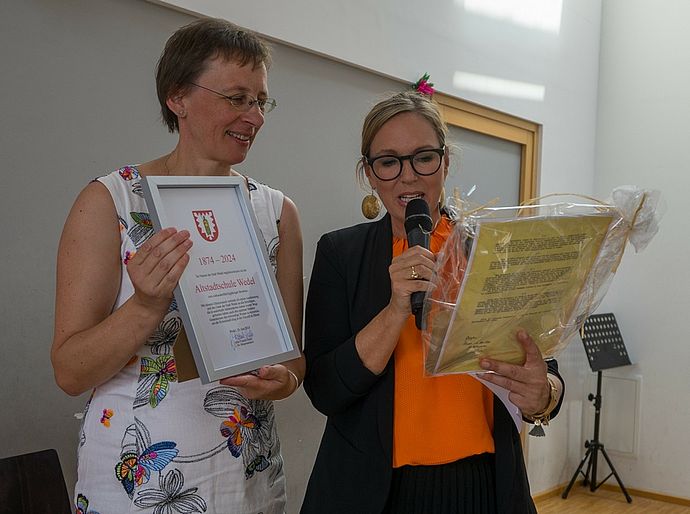 Die 2. stellvertretende Bürgermeisterin der Stadt Wedel, Julia Fisauli (r.), übergab bei ihren Glückwünschen an Schulleiterin Andrea Spangenberg eine Urkunde und eine "Dienstanweisung für Hauptleherer" vom Anfang des vergangenen Jahrhunderts. Foto: Stadt Wedel/Kamin