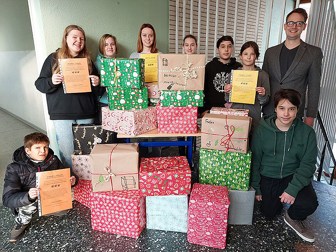Eine Gruppe von Jungen und Mädchen mit vielen großen Geschenkpakete und ihr Lehrer am Rande des Bildes