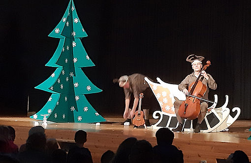 Zwei Männer auf der Bühne mit Rentierschlitten und Papp-Weihnachtstanne