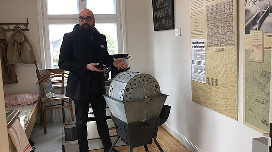 Museumsleiter Holger Junker steht in den Räumlichkeites des Stadtmuseums, rechts neben ihm eine altertümliche Waschmaschine aus dem Jahr 1930 und erklärt.