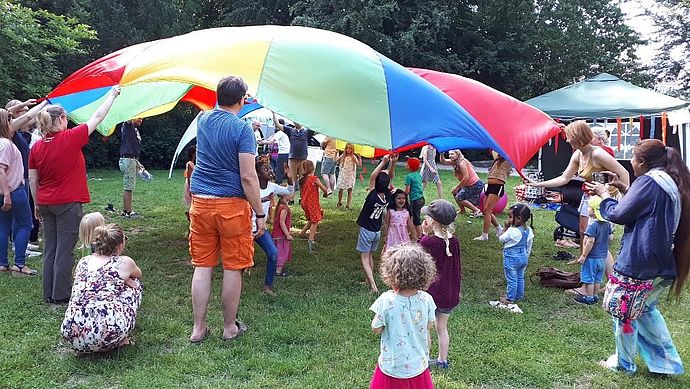 Kinder und Erwachsene spielen mit einem bunten fallschirmartigen Tuch