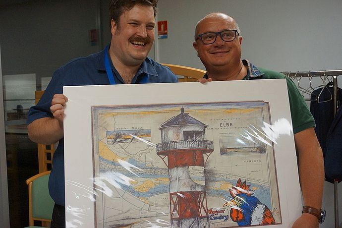 Sven Kamin übergab dem Bürgermeister von Caudry Frédéric Bricout ein eigens für den Anlass angefertigtes Bild des Wedeler Künstlers Ole West – komplett mit dem französischen Hahn. Foto: Stadt Wedel
