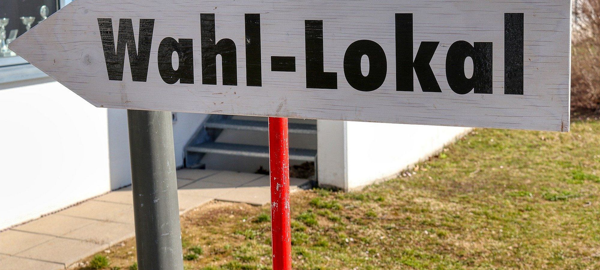 Schild mit der Aufschrift Wahllokal, was nach links zum Wahlort zeigt.